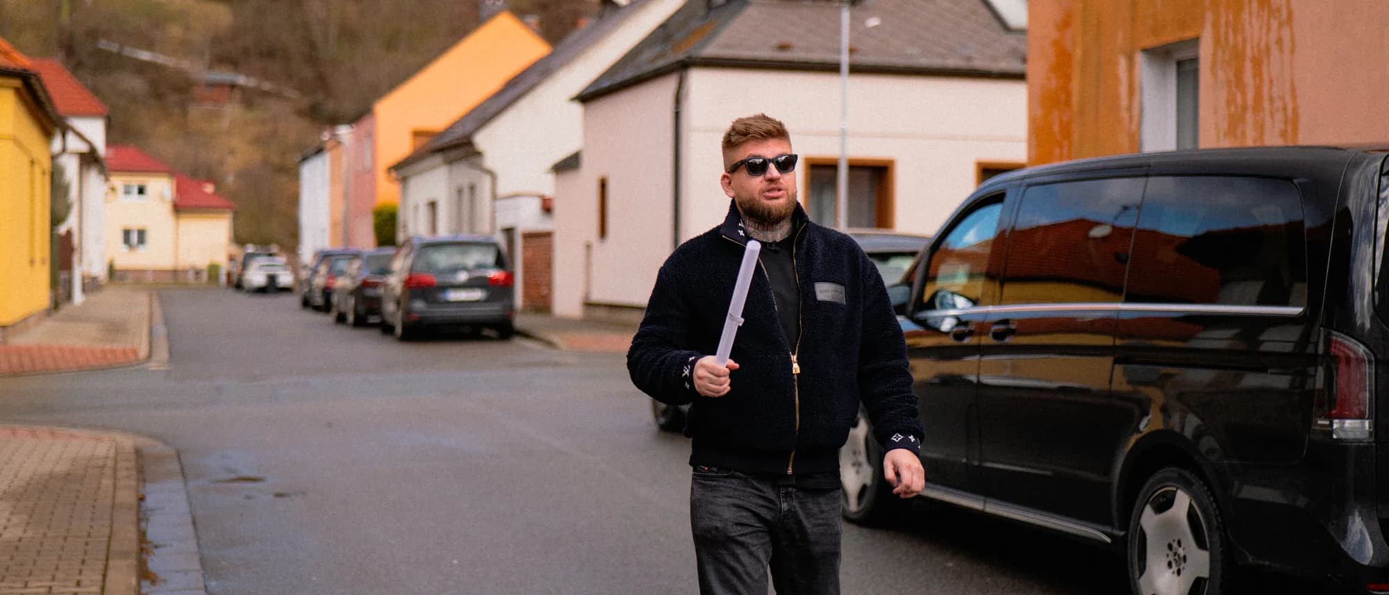 Maxim Ponomarenko prochází ulicí rodinných domů s plánem nemovitosti v ruce