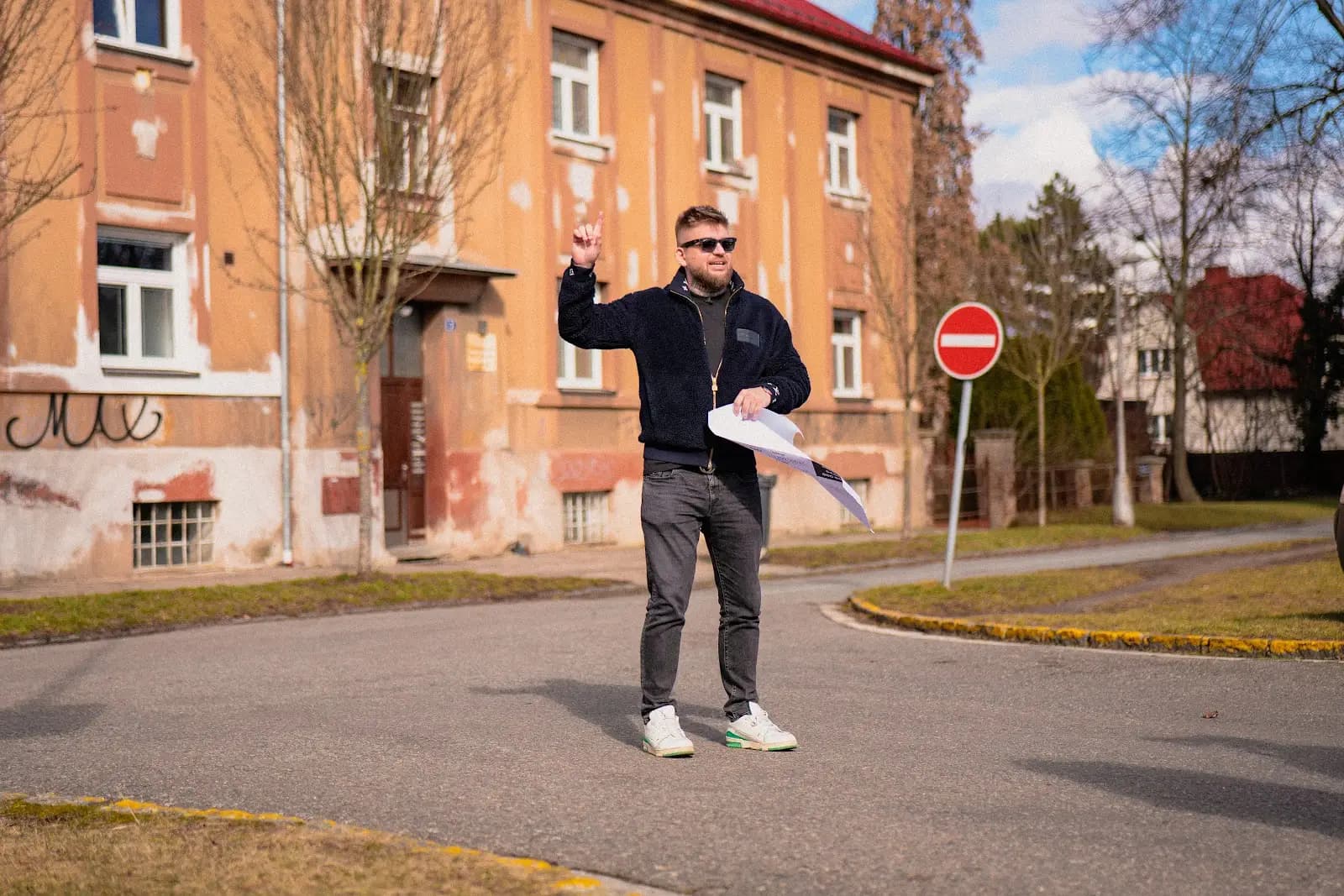 Maxim Ponomarenko před cihlovým činžovním domem, v ruce podklady k nemovitosti